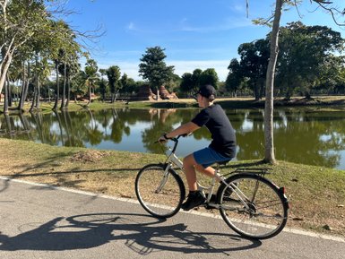 Junge fährt mit Fahrrad durch die Anlage von Wat Mahathat in Sukhothai - Thailand Familienreise