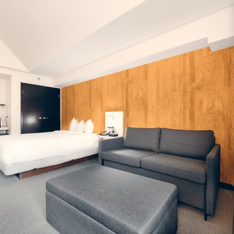 Ein modernes Hotelzimmer mit einem großen Bett, einem grauen Sofa und einer Holzverkleidung an der Wand.