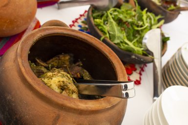 Ein traditioneller Pachamanca-Eintopf in einem Tontopf, gefüllt mit zartem Fleisch und Kräutern, umgeben von frischem Salat.