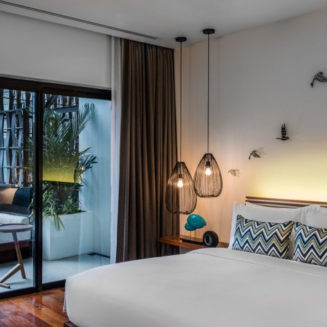 Ein modernes Schlafzimmer mit einem großen Bett, stilvollen Lampen und einem Blick auf einen Balkon mit Pflanzen und Sitzgelegenheiten.