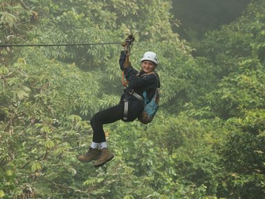 Frau schwebt lachend an einer Zipline durch die Baumkronen des Selvatura Parks – Costa Rica Reise mit Kindern