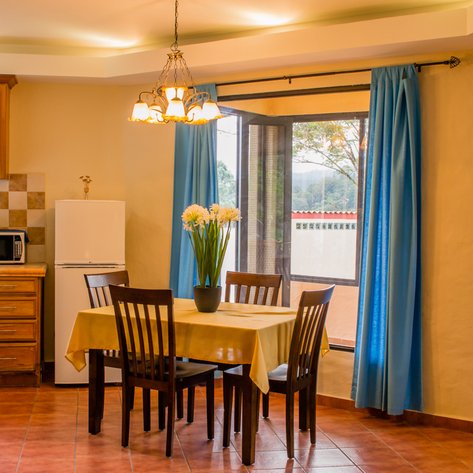 Eine gemütliche Küche mit einem Esstisch, umgeben von Stühlen, und einer großen Fensterfront, die Tageslicht hereinlässt.