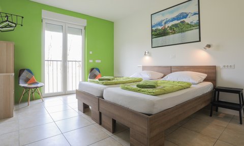 Ein helles Schlafzimmer mit zwei Betten, frischen grünen Decken und einem großen Fenster, das auf einen schönen Ausblick zeigt.
