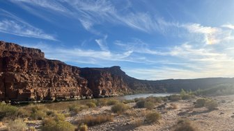 Die majestätischen roten Felsen erheben sich über den ruhigen Colorado River, umgeben von sanften Sträuchern und Gras.