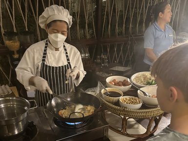 Kind beobachtet aufmerksam eine einheimische Köchin bei der Zubereitung von thailändischen Gerichten – Thailand Familienreise