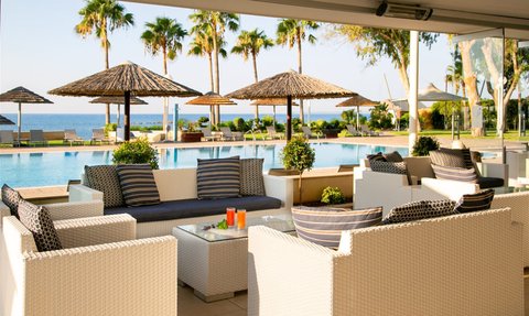 Ein eleganter Außenbereich mit weißen Sofas und einem Glastisch, umgeben von Palmen und einem Pool mit Meerblick.