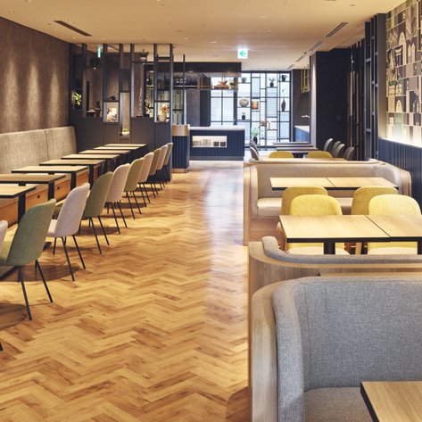 Ein modernes Restaurant mit eleganten Holztischen und bequemen Stühlen, das eine einladende Atmosphäre ausstrahlt.