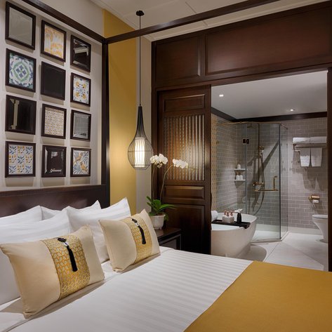 Ein elegantes Hotelzimmer mit einem großen Bett, dekorativen Kissen und einer stilvollen Wand mit gerahmten Fliesen.