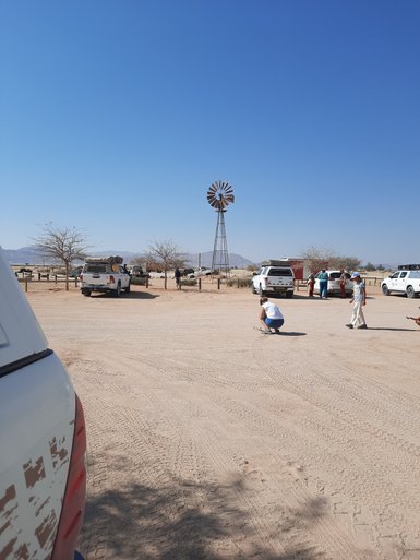 Mehrere Fahrzeuge stehen auf einem sandigen Parkplatz im Dorf Solitaire - Namibia mit Kindern