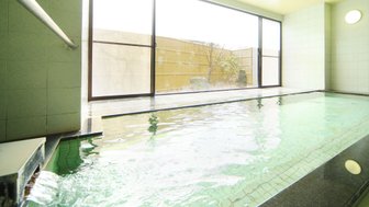 Ein entspannendes Onsen mit klarem Wasser, das sanft plätschert, umgeben von großen Fenstern und einem ruhigen Außenbereich.