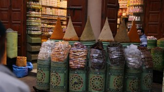 Bunte Gewürze in kegelförmigen Behältern stehen in einem lebhaften Markt, umgeben von Regalen mit verschiedenen Produkten.
