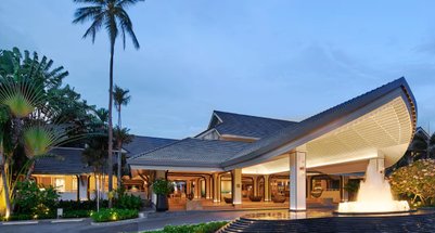Der Eingangsbereich des Hotels Melia Koh Samui zeigt eine moderne Architektur mit einem beeindruckenden Wasserfall und Palmen.