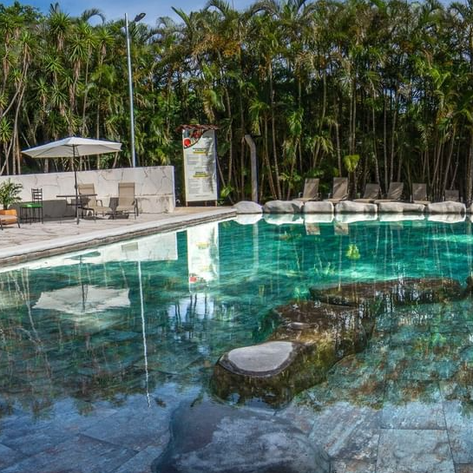 Ein glitzernder Pool spiegelt die umgebenden Palmen und den blauen Himmel wider, umgeben von bequemen Liegen.