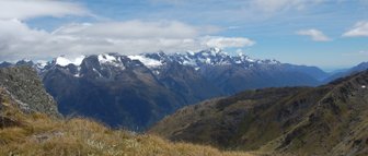 Eine weite Aussicht auf die majestätischen Berge des Mount Aspiring Nationalparks, umgeben von sanften Grasflächen.