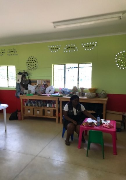 In einem hellen Raum sitzt eine Frau an einem kleinen Tisch, umgeben von bunten Materialien und Werkzeugen.