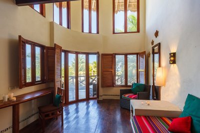 Ein helles Zimmer mit großen Fenstern, das eine entspannte Atmosphäre mit bunten Kissen und Holzdetails ausstrahlt.