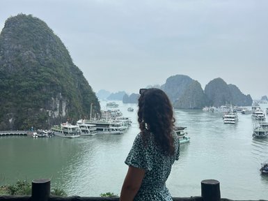 Eine Frau in einem blauen Kleid steht an einem Geländer und blickt auf die beeindruckende Halong-Bucht mit ihren Felsen.