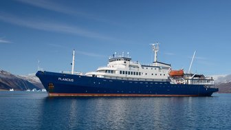 Das Forschungsschiff Plancius liegt ruhig im Wasser, umgeben von majestätischen Bergen und Eisbergen im Hintergrund.