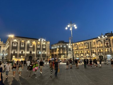 Die belebte Piazza Duomo in Catania ist bei Nacht erleuchtet, mit Menschen, die fröhlich umhergehen und die Atmosphäre genießen.