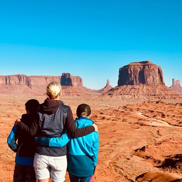 Drei Personen stehen mit dem Rücken zur Kamera und betrachten die beeindruckenden Felsformationen von Monument Valley.