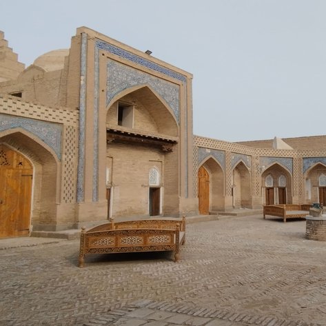 Ein historischer Innenhof mit kunstvoll verzierten Gebäuden und Holzsitzgelegenheiten, umgeben von kargem Gelände und kahlen Bäumen.