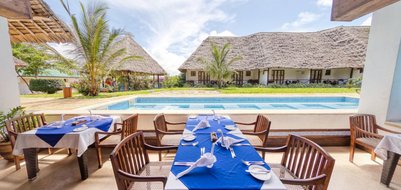 Ein eleganter Restaurantbereich mit blauen Tischdecken, umgeben von Palmen und einem glitzernden Pool im Hintergrund.