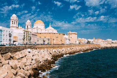 Die Küstenlinie von Cádiz zeigt historische Gebäude und eine beeindruckende Kathedrale vor einem strahlend blauen Himmel.
