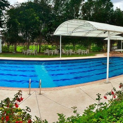 Ein klarer Pool mit blauen Wasser und einem überdachten Bereich, umgeben von grünen Bäumen und bunten Blumen.