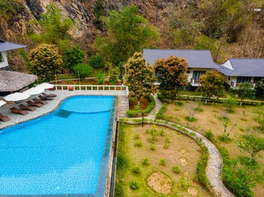 Ein atemberaubender Blick auf einen blauen Pool, umgeben von üppigem Grün und modernen Bungalows in einer ruhigen Berglandschaft.
