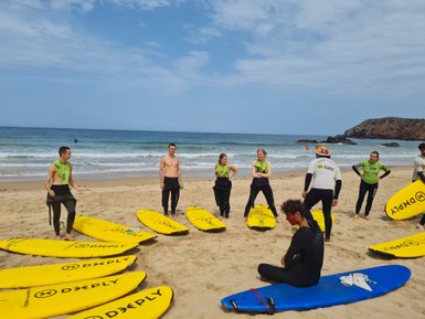 Eine Gruppe von Surfschülern steht am Strand, umgeben von gelben Surfbrettern und dem Ozean im Hintergrund.