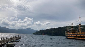 Ein Piratenschiff fährt auf dem ruhigen Wasser des Ashi-Sees, umgeben von grünen Bergen und dramatischen Wolken.