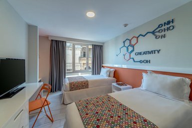 Zwei Einzelbetten mit bunten Bettüberwürfen in einem modernen Hotelzimmer, das Kreativität und Stil ausstrahlt.