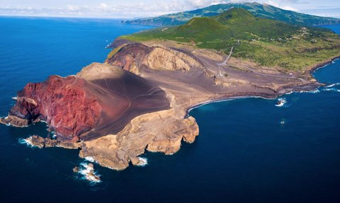 Eine beeindruckende Küstenlandschaft mit roten Klippen, die ins tiefblaue Wasser des Ozeans fallen.