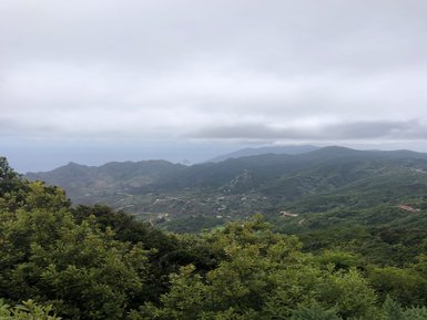 Eine weite Aussicht auf grüne Berge und Hügel, die unter einem bewölkten Himmel liegen, mit dem Ozean in der Ferne.