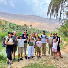 Gruppe posiert für Foto im Wadi Shab mit Bergen im Hintergrund – Oman Familienreise