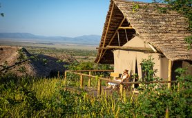 Eine Frau sitzt entspannt auf der Veranda eines Zeltes und genießt die Aussicht auf die weite Landschaft des Ngorongoro-Kraters.