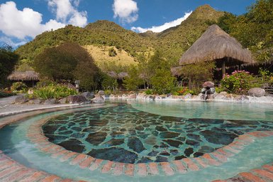 Ein klarer Pool mit einem einzigartigen Steinmuster, umgeben von üppiger Vegetation und majestätischen Bergen im Hintergrund.