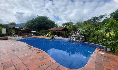 Ein einladender Pool mit klarem Wasser, umgeben von üppigem Grün und einem Holzpavillon im Hintergrund.