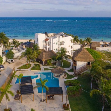 Ein Blick auf das Hotel Ojo de Agua, umgeben von Palmen und einem einladenden Pool, mit dem Meer im Hintergrund.
