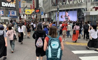Eine belebte Straße in Shibuya, Tokio, mit vielen Fußgängern und einem großen Starbucks-Schild im Hintergrund.