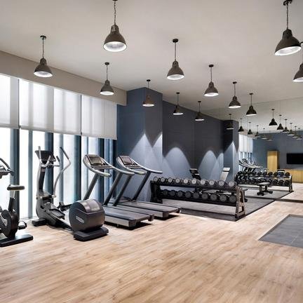 Ein moderner Fitnessraum mit verschiedenen Trainingsgeräten, großen Fenstern und warmem Holzfußboden.