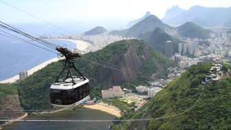 Eine Seilbahn schwebt über der Küste von Rio de Janeiro, mit Aussicht auf den Strand und die umgebenden Berge.