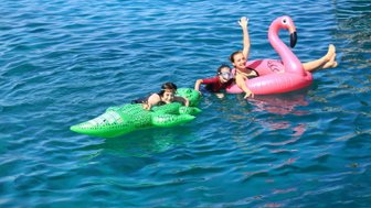 Drei Kinder genießen einen sonnigen Tag im Wasser, während sie auf bunten Schwimmreifen spielen und lachen.