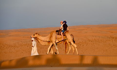 Beduin führt Kamele mit Mutter und Tochter durch die Wüste – Oman Familienreise