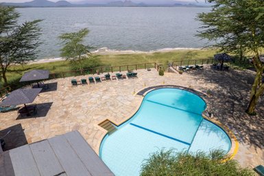 Ein einladender Pool mit blauen Wasser und einer Steinoberfläche, umgeben von Liegen und Sonnenschirmen am Ufer eines Sees.