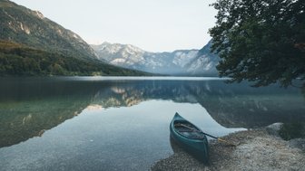 Ein ruhiger See umgeben von majestätischen Bergen, mit einem Kanu, das sanft am Ufer liegt und die Landschaft spiegelt.