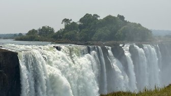 Die majestätischen Victoriafälle stürzen mit kraftvollem Wasser in die Tiefe, umgeben von üppigem Grün und Nebel.