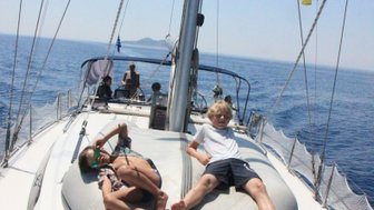 Zwei Kinder entspannen auf einem Boot, während das Wasser glitzert und die Sonne scheint, umgeben von einem klaren blauen Himmel.