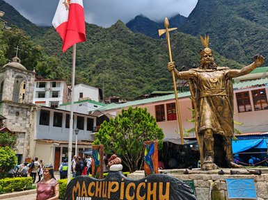 Eine goldene Statue eines Inka-Herrschers steht stolz vor den majestätischen Anden, umgeben von einem lebhaften Dorf.