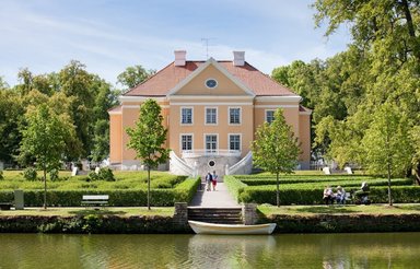 Ein elegantes, gelbes Herrenhaus mit einem gepflegten Garten und einem ruhigen Teich im Vordergrund, umgeben von Bäumen.